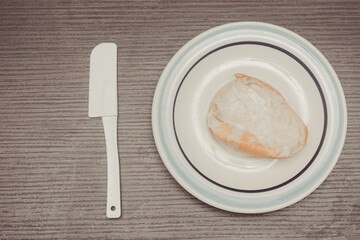 French bread, individual portion ready to spread on white ceramic plate with isolated wooden background. butter knife