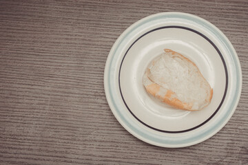 French bread, individual portion ready to spread on white ceramic plate with isolated wooden background.