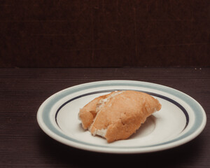 French bread, individual portion on white ceramic plate with isolated wooden background. lateral view
