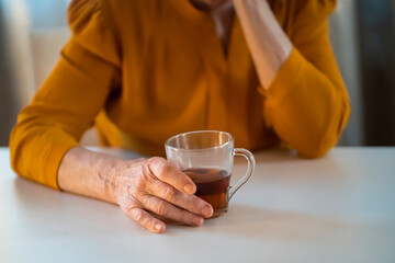 Old woman drinks tea in her cozy house.