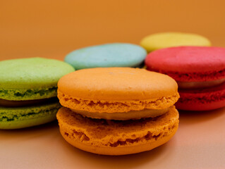 Close-up of French dessert for coffee. Multicolored macarons or macaroons on orange background. High quality photo