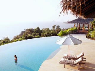 A woman stands in a luxury infinity pool overlooking  Phang Nga Bay, Yao Noi, Thailand.