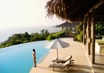 A woman stands by a luxury infinity pool overlooking  Phang Nga Bay, Yao Noi, Thailand.