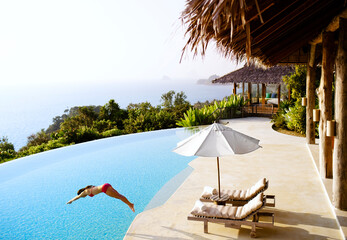 A woman dives into a private luxury infinity pool  overlooking Phang Nga Bay, Yao Noi, Thailand.