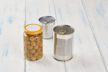Iron tin can with tab opener and olives in a glass jar on the white  wooden table.
