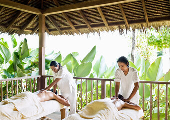A couple receives simultaneous oil massages in an open-air treatment room of a private pool villa. Yao Noi. Thailand.