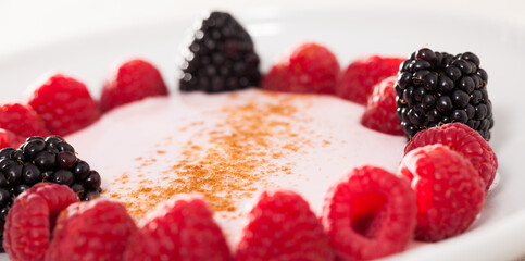 raspberries and blackberries laid out on a white plate in circle with yogurt and cinnamon