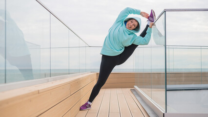 Caucasian woman in a sweatshirt stretches on the split outdoors. 