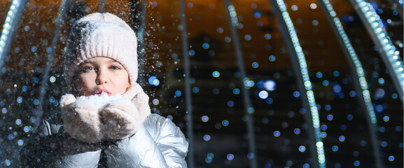 Girl and snow. Girl blowing on palms with snow at night with blue backlight and blurry lights. Banner