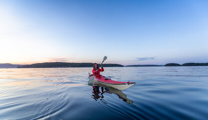 Fototapeta na wymiar Adventurous Woman on Sea Kayak paddling in the Pacific Ocean. Sunny Summer Sunset. Taken near Victoria, Vancouver Islands, British Columbia, Canada. Concept: Sport, Adventure