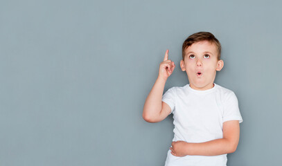 European handsome little boy is surprised, inspired, i have an idea, raise your index finger up, copy space, isolated on gray background. schoolboy