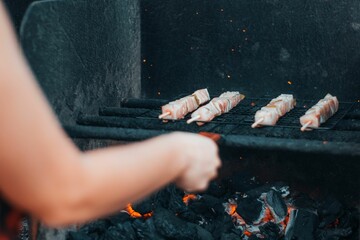 Closeup view of a Spanish girl cooking meat on a grill mesh in a park in daylight