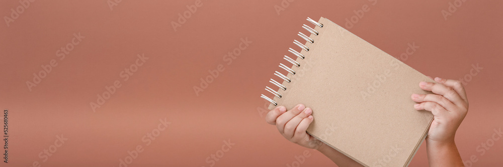 Wall mural notepad in hand. blank notepad in the hands of a child on a red background. hands hold a book withou