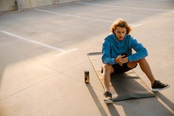 Young man using cellphone while working out on fitness mat at parking