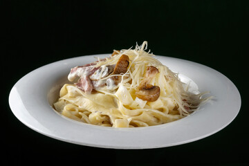Spaghetti with ham and champignon mushrooms sprinkled with cheese. On a white plate, black background. copyspace.