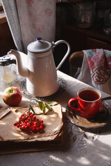 Still life in old rustic kitchen with a cup of tea and a bunch of red rowan and red apples, autumn morning tea concept.