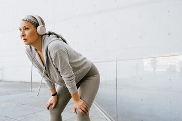 Asian mature woman in headphones standing during workout