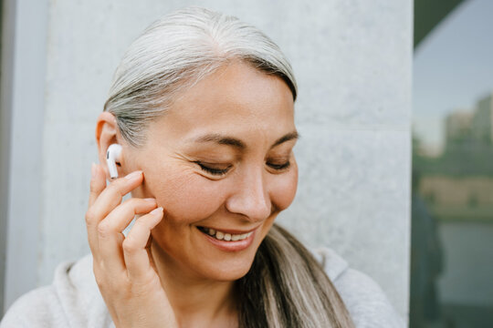 Asian mature woman in earphones laughing while listening music
