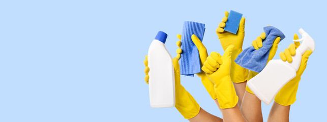 hand with yellow rubber glove holding cleaning supplies on blue background. banner with copy space