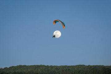 Silhouette of paraglider flying above trees with full moon rising behind him