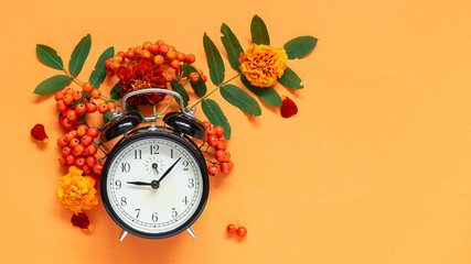 Hello, Autumn. Autumn composition of rowan, flowers and alarm clock on orange background with copy...