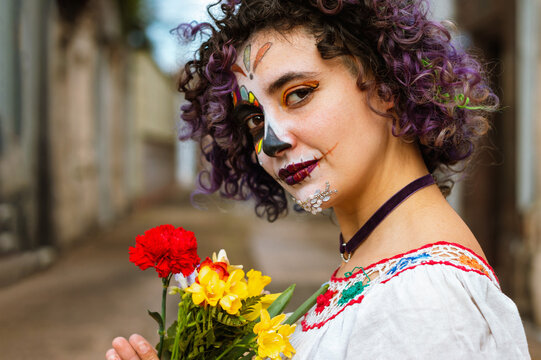 portrait of young latin woman holding flowers in the cemetery with La Calavera Catrina makeup