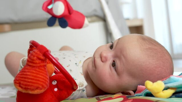big-eyed baby plays with her toys lying quietly in her play area,4k video, slow motion