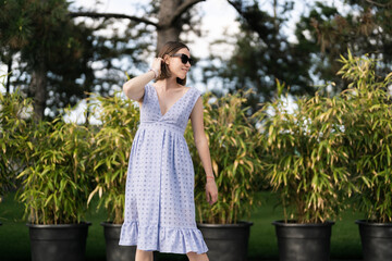 Cheerful caucasian woman in blue dress posing ourdoors in motion, on plants background