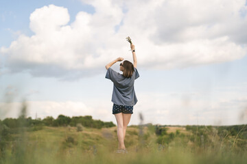 Fototapeta na wymiar Carefree young woman daydreaming in nature touching beautiful clouds with finger