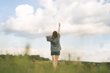 Carefree young woman daydreaming in nature touching beautiful clouds with finger