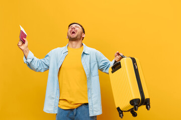 Overjoyed young tanned handsome man in blue shirt raise hands with passport plane tickets and suitcase up posing isolated on yellow studio background. Copy space Banner Mockup. Trip journeys concept