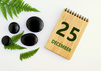 December 25 . 25th day of the month, calendar date. Notepad, black stones, green leaves. Winter...