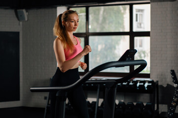Fototapeta na wymiar Athletic build girl doing cardio training exercise by jogging on a treadmill in the gym