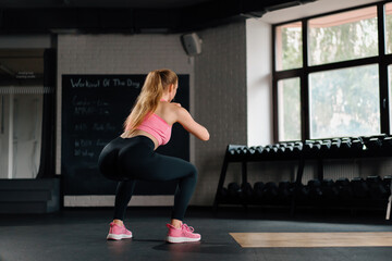 Naklejka na ściany i meble Athletic woman doing squats with a weight in the gym. Mobility and Leg Exercise Workout