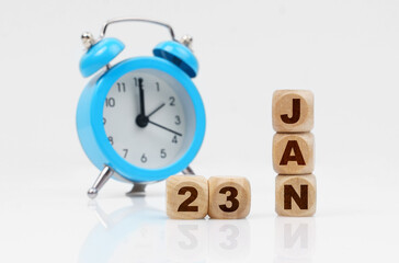 Wooden cube calendar for January 23, next to a blue alarm clock.