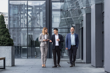 Three diverse business people walking and talking focused and thoughtful seriously outside office...