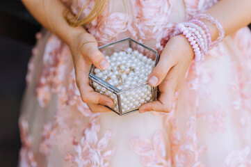 A girl, a child in a lace dress holds a glass box with beads and gold rings at the ceremony...