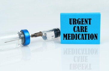 On a white reflective surface there is a syringe with an ampoule and a plate with the inscription URGENT CARE MEDICATION