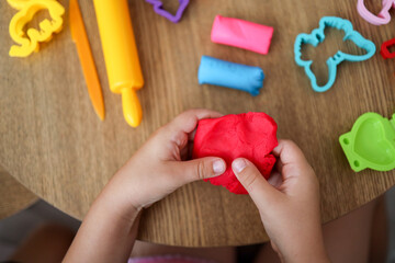 Baby hands holding and kneading red modeling clay on white table background. Closeup. Toddler...