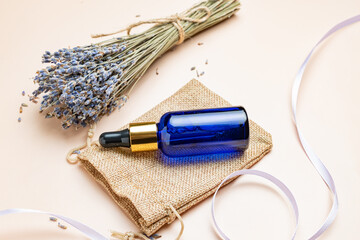 Lavender essential oil in blue glass bottle with pipette. Bottle with fragrant oil and lavender flowers on beige background. mockup of lavender essential oil