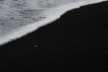 Waves and sand on ocean coastline. Icelandic black sand. Background, pattern, volcanic black sea sand.