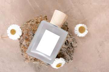 Transparent bottle of perfume with white labels on stone podium on beige terracotta background with dry flower. Fragrance presentation, Minimal cosmetic packaging mockup, flat lay, top view, above