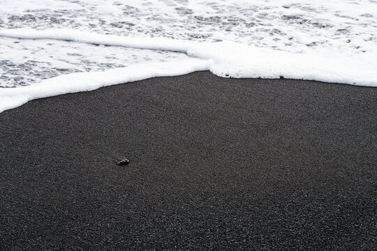 Waves and sand on ocean coastline. Icelandic black sand. Background, pattern, volcanic black sea sand.