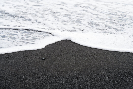 Waves and sand on ocean coastline. Icelandic black sand. Background, pattern, volcanic black sea sand.