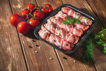 Raw lula kebab wrapped in bacon in a plate on a vintage table with tomato and dill