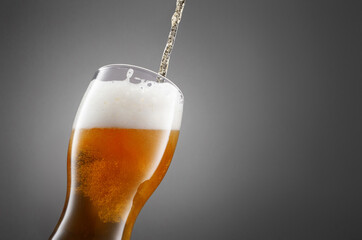 Stream of draught beer in glass on a granite stone. Glass of fresh and cold beer on gray dark...