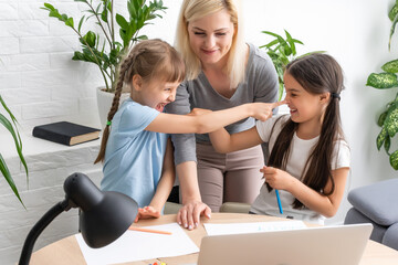 Beautiful young mother helping her daughters with homework.