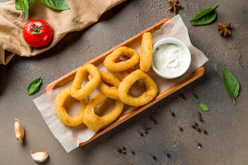 Rings of squid in batter with sauce on brown concrete table top view