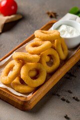 Onion rings in batter with sauce on brown concrete table, vertical