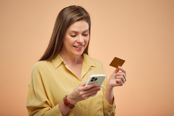 Smiling woman using smartphone and credit card, isolated portrait on yellow background.